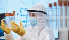 Científica en traje limpio con tubos de ensayo que estudia el coronavirus - foto de stock
