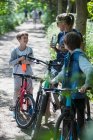 Мать и сыновья пьют воду на велосипеде в солнечном парке — стоковое фото