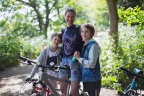 Retrato mãe feliz e filhos desfrutando de passeio de bicicleta no parque ensolarado — Fotografia de Stock
