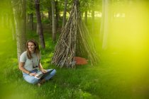 Smiling woman using laptop outside branch teepee in woods — Stock Photo