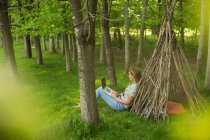 Mulher com laptop relaxante em teepee ramo na floresta — Fotografia de Stock