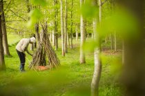 Donna anziana che fa ramo teepee nel bosco — Foto stock