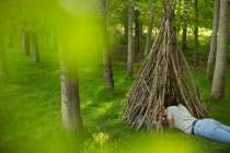 Woman relaxing in branch teepee in woodland — Stock Photo