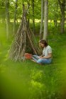Femme avec ordinateur portable relaxant à la branche tipi dans les bois — Photo de stock