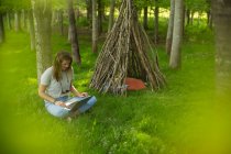 Young woman using laptop at branch teepee in woods — Stock Photo