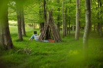 Young woman using laptop at branch teepee in woodland — Stock Photo