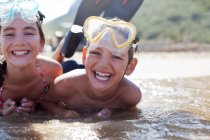 Begeistertes Geschwisterpaar trägt Schutzbrille und liegt im Meer — Stockfoto