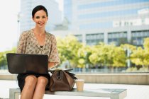 Усміхнена бізнес-леді з ноутбуком на відкритому повітрі — стокове фото