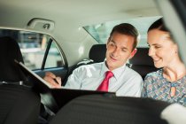 Бизнесмен и бизнесвумен, работающие на заднем сиденье автомобиля — стоковое фото