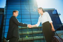Businessman and businesswoman shaking hands below highrise — Stock Photo