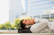 Empresário deitado na pasta e falando no celular no parque urbano — Fotografia de Stock