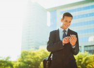 Businessman text messaging outside urban building — Stock Photo