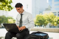 Улыбающийся бизнесмен, работающий на ноутбуке в городском парке — стоковое фото