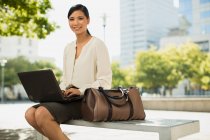 Усміхнена бізнес-леді співає ноутбук у міському парку — стокове фото
