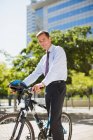 Homme d'affaires souriant avec vélo et casque dans un parc urbain — Photo de stock
