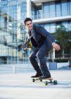 Улыбающийся бизнесмен катается на скейтборде возле городского здания — стоковое фото