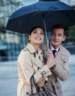 Empresário e empresária assistindo chuva sob guarda-chuva — Fotografia de Stock