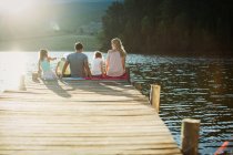 Família sentada na beira da doca sobre o lago — Fotografia de Stock