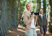 Усміхнена жінка з цифровою камерою в лісі — стокове фото