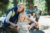 Smiling mother and daughter with bicycle in woods — Stock Photo