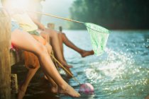 Сім'я на причалі з рибальськими сітками, що занурюються ногами в озеро — стокове фото