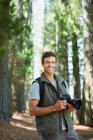 Усміхнений чоловік з цифровою камерою в лісі — стокове фото