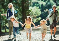 Sonriente familia cogida de la mano y corriendo en el bosque - foto de stock