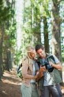 Sonriente pareja mirando a la cámara digital en el bosque - foto de stock
