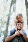 Улыбающийся отец носит дочь на плечах в лесу — стоковое фото