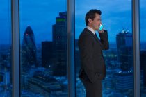Empresario hablando por teléfono celular en ventana urbana por la noche - foto de stock