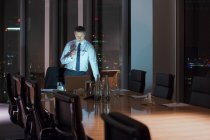 Businessman working at laptop in conference room at night — Stock Photo