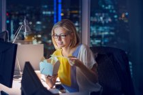 Businesswoman eating take out food at desk in office at night — Stock Photo