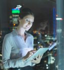 Geschäftsfrau nutzt nachts digitales Tablet im Stadtfenster — Stockfoto