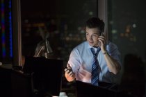 Businessman talking on cell phone in office at night — Stock Photo