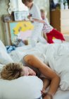 Mother sleeping in bed while her sons playing in background — Stock Photo