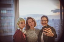 Smiling businesswomen taking selfie at highrise office window — Stock Photo