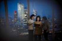 Gente de negocios con tableta digital trabajando hasta tarde en la ventana de rascacielos - foto de stock