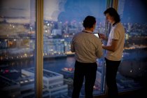 Geschäftsleute mit digitalem Tablet arbeiten spät am Bürofenster eines Hochhauses — Stockfoto