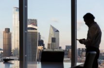 Uomo d'affari che utilizza lo smart phone alla finestra dell'ufficio grattacielo, Londra, Regno Unito — Foto stock