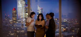 Gente de negocios con tableta digital trabajando hasta tarde en la ventana de rascacielos - foto de stock