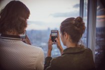 Giovane coppia con smartphone che fotografa il tramonto alla finestra del grattacielo — Foto stock