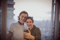 Happy young couple taking selfie at highrise window — Stock Photo