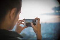 Woman with camera phone photographing sunset at highrise window — Stock Photo