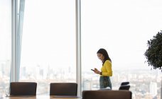 Businesswoman using smart phone in highrise conference room — Stock Photo