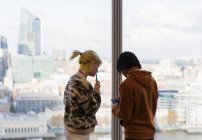 Gente de negocios usando teléfono inteligente en la ventana urbana de oficinas de gran altura - foto de stock