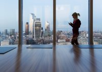 Donna d'affari che utilizza lo smart phone alla finestra dell'ufficio grattacielo, Londra, Regno Unito — Foto stock