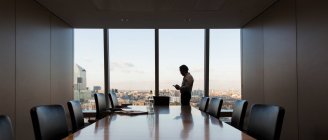 Geschäftsmann mit Smartphone am Fenster eines Konferenzraums im Hochhaus — Stockfoto