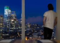 Бизнесмен, работающий поздним вечером у окна высотного офиса, Лондон, Великобритания — стоковое фото