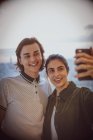 Feliz joven pareja tomando selfie con cámara de teléfono en la ventana - foto de stock