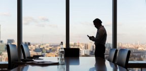 Uomo d'affari che utilizza lo smart phone alla finestra dell'ufficio grattacielo, Londra, Regno Unito — Foto stock